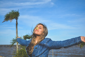 Woman in denim jacket in the sun wearing sunscreen on her nose. Posing near a pier and with trees in the background.